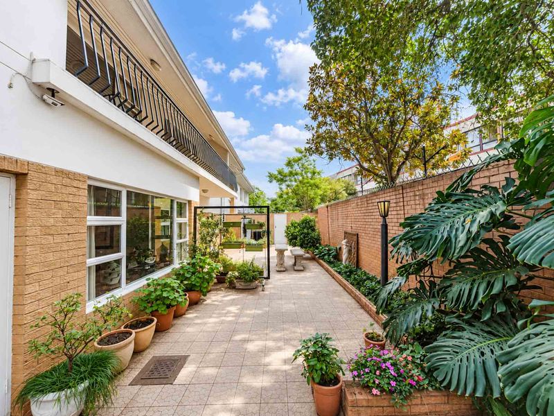 A well-maintained rear patio area featuring tiled flooring, a brick boundary wall, and access to the upper-level balcony.