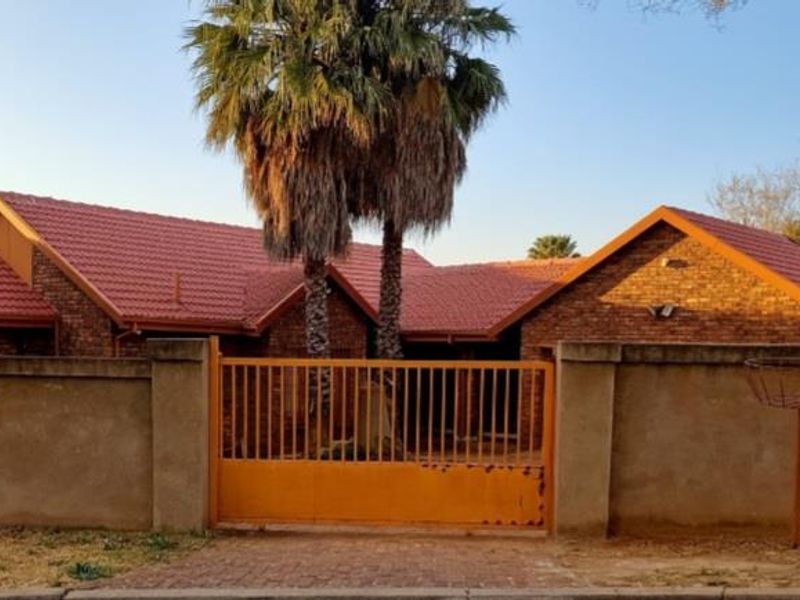 Front view of a face brick house featuring a tiled roof, perimeter wall, and a metal driveway gate.