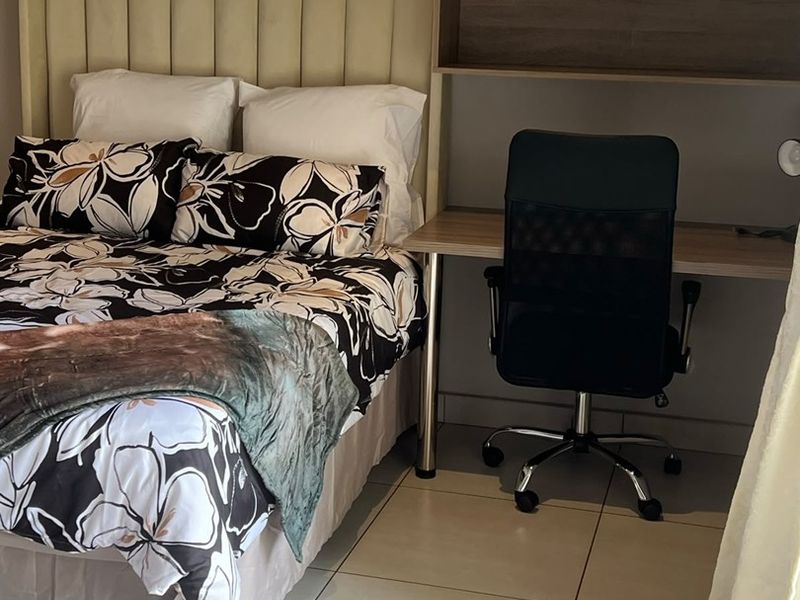 A bedroom featuring tiled flooring and a built-in desk with overhead shelving, providing a functional workspace within the sleeping area.