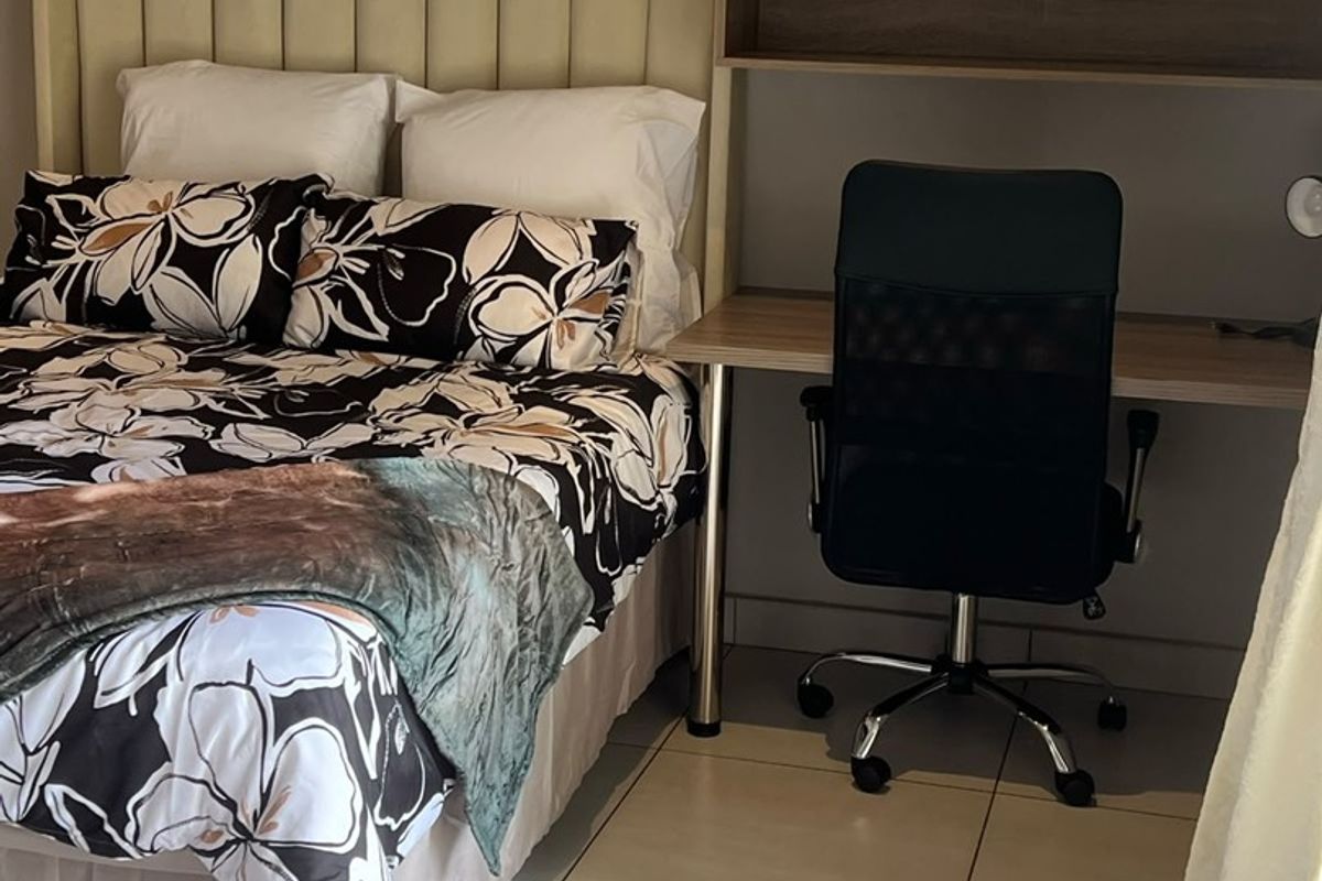 A bedroom featuring tiled flooring and a built-in desk with overhead shelving, providing a functional workspace within the sleeping area.