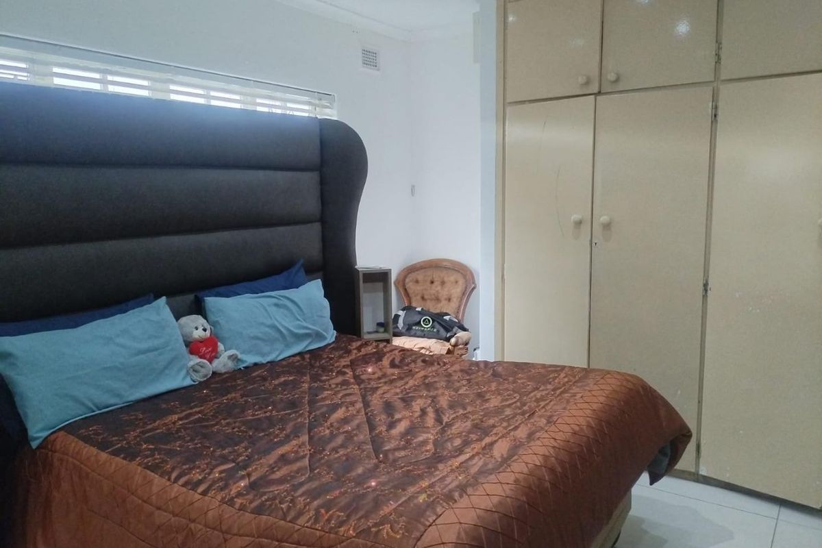 A bedroom featuring built-in cupboards, tiled flooring, and venetian blinds, offering a functional space with potential for cosmetic updates.
