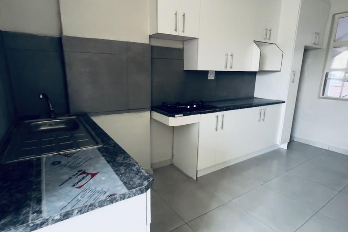 A clean, modern kitchen featuring white cabinetry, dark laminate countertops, a gas hob, and neutral tiled flooring.
