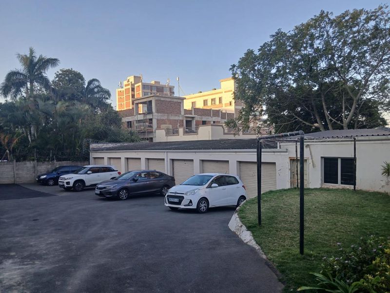Exterior view of the apartment complex showing a row of garage units, paved driveway, and surrounding landscaped garden area.