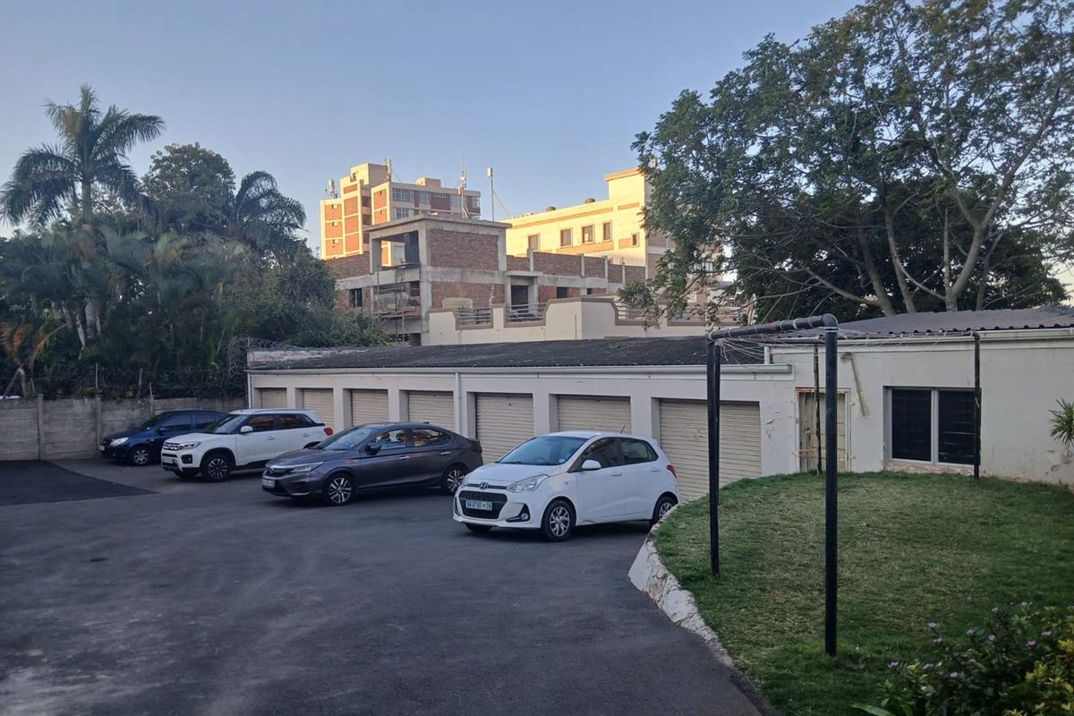 Exterior view of the apartment complex showing a row of garage units, paved driveway, and surrounding landscaped garden area.