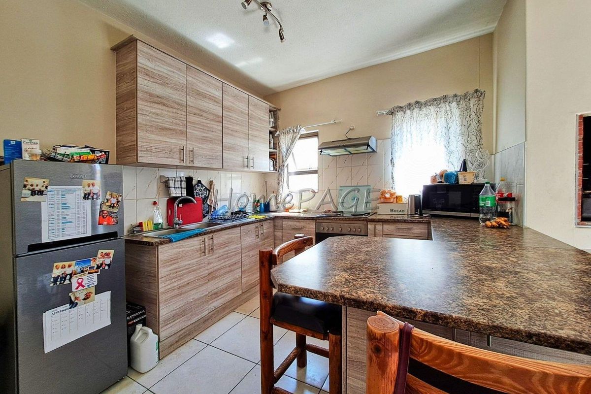 A functional kitchen featuring wood-look laminate cabinetry, granite-style countertops, tiled flooring, and a built-in extractor fan.