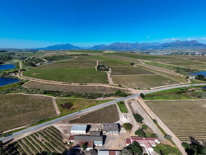 An expansive aerial view of a large farm property featuring extensive vineyards, multiple dams, and various agricultural outbuildings set against a mountain backdrop.