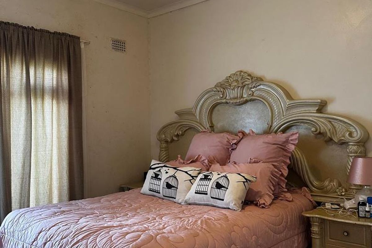 A bedroom featuring a large ornate headboard, window with curtains, and a ceiling-mounted light fixture.