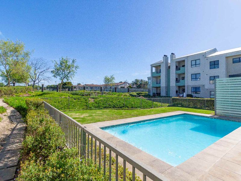 A well-maintained outdoor pool area featuring a paved patio, metal fencing, and a landscaped garden set within an apartment complex.