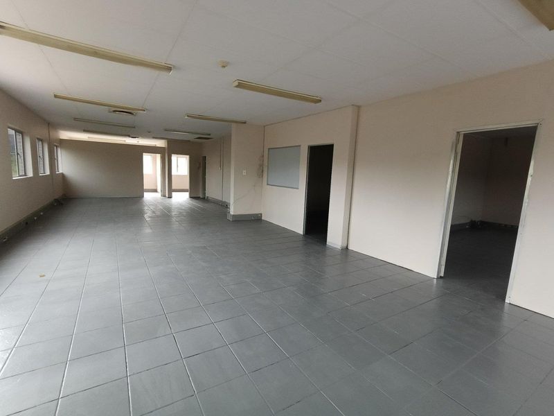 An expansive, empty industrial office space featuring tiled flooring, suspended ceilings with fluorescent lighting, and multiple internal access points.