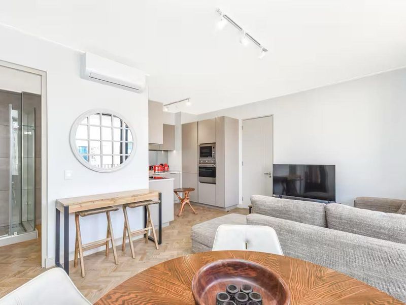 Modern open-plan living area featuring herringbone timber flooring, integrated kitchen appliances, split-system air conditioning, and direct access to a contemporary bathroom.