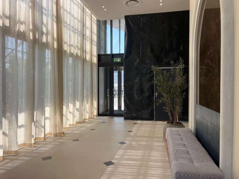 Spacious modern entrance lobby featuring high ceilings, large windows with floor-to-ceiling curtains, and tiled flooring.