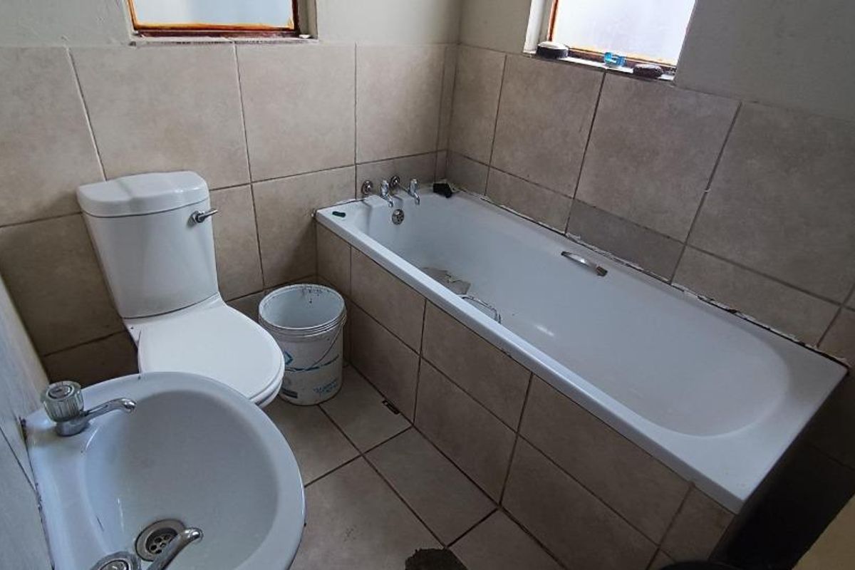A compact bathroom featuring a standard bathtub, pedestal basin, and toilet with neutral wall and floor tiling.