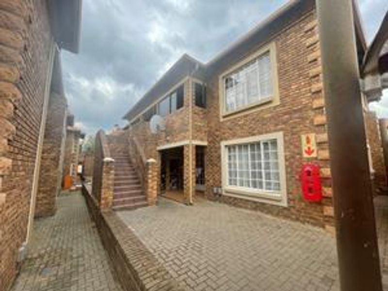 Exterior view of a facebrick cluster unit featuring a paved driveway, external staircase, and secure window fittings.