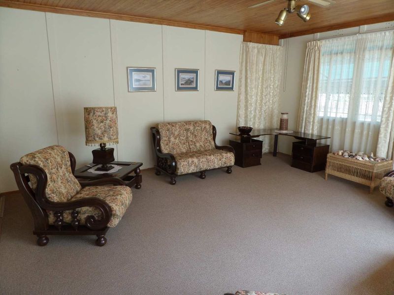 A living room featuring timber ceiling paneling, a ceiling fan, and carpeted flooring, offering a dated aesthetic ready for modernization.