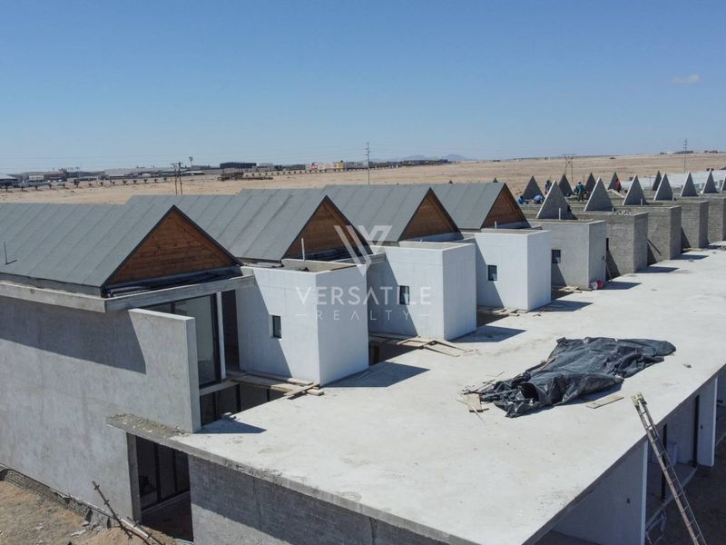 Aerial view of a townhouse development under construction, featuring multiple units with pitched roofs and unfinished concrete structures.