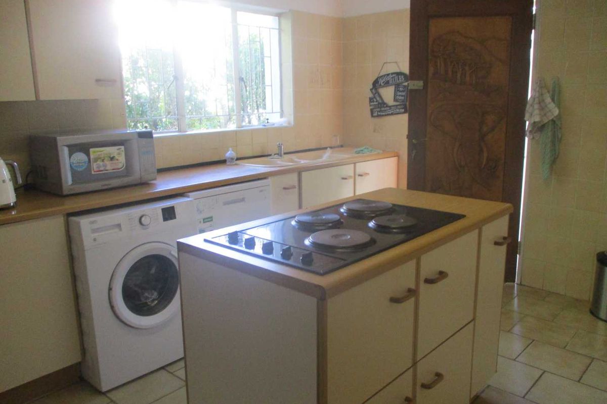 Functional kitchen featuring a central island with a built-in electric hob, tiled flooring, and ample cabinetry for storage.