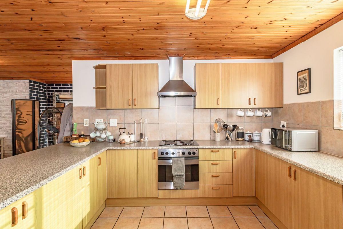 A functional kitchen featuring light wood cabinetry, granite-look countertops, a stainless steel oven and extractor, and a distinctive timber-clad ceiling.
