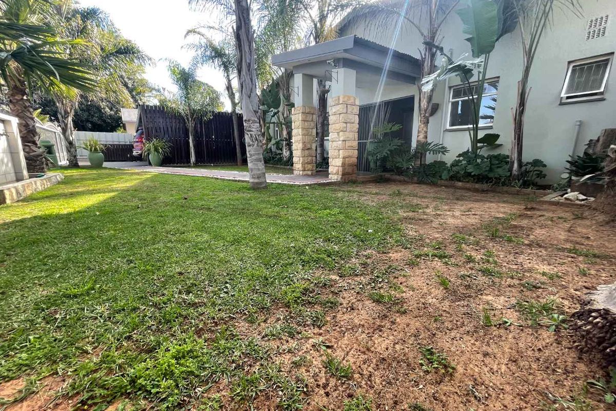 Rear garden view featuring a covered patio with stone-clad pillars, paved walkway, and established landscaping.