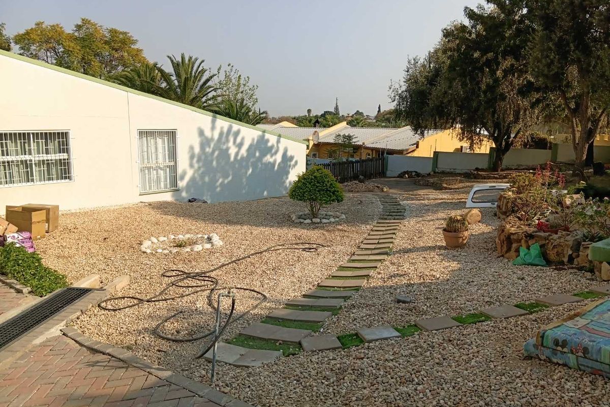A rear garden area featuring gravel landscaping, a paved stone walkway, and security bars on the building windows.