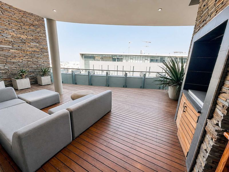 Spacious penthouse balcony featuring timber decking, stacked stone feature walls, and a built-in braai area with panoramic urban views.