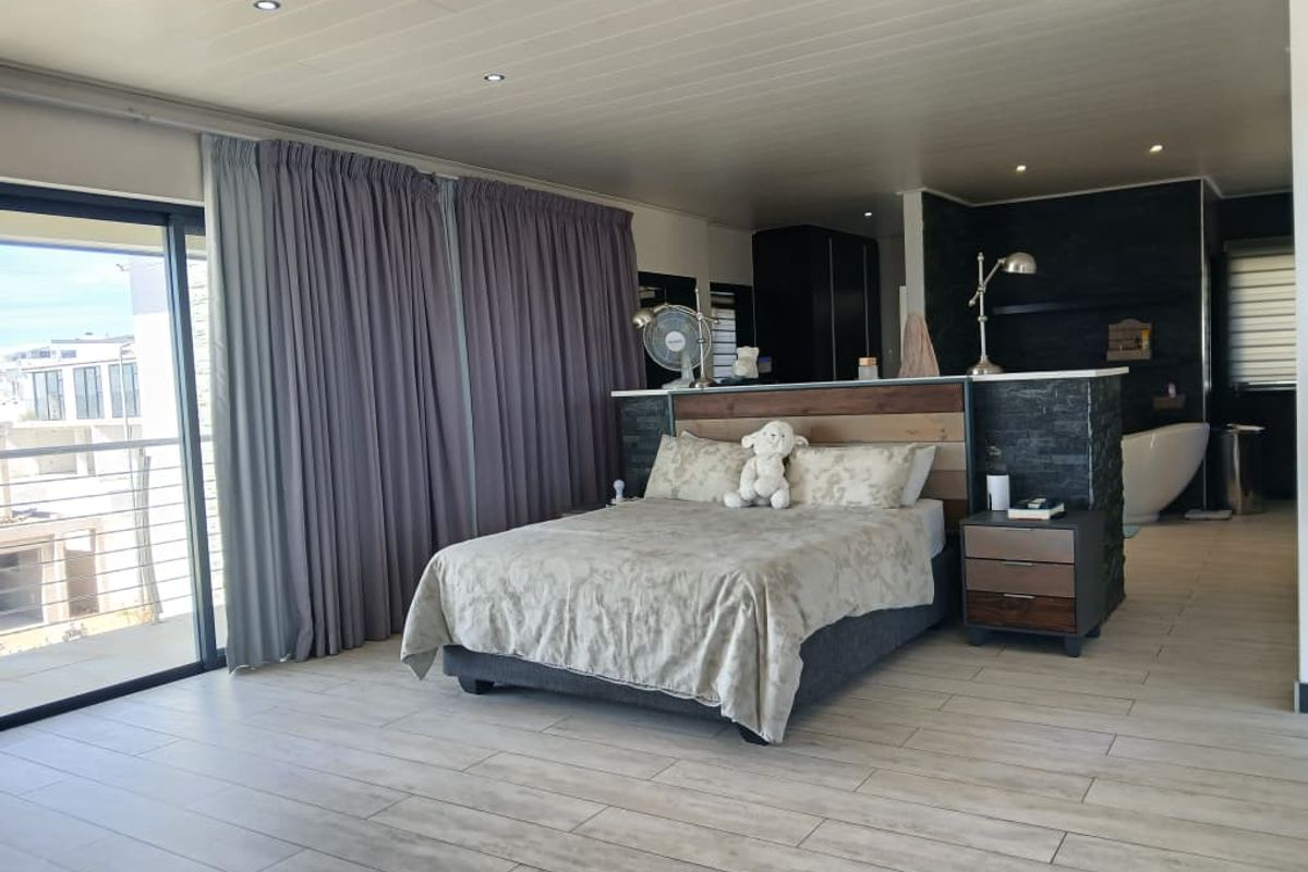 Spacious open-plan bedroom featuring a modern partition wall, integrated en-suite bathroom area, wood-look tile flooring, and large sliding doors leading to a balcony.