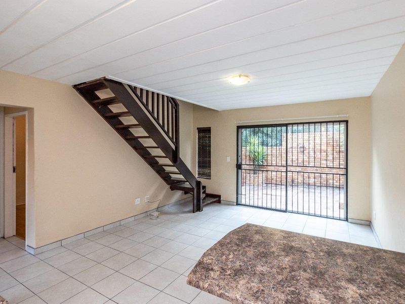Open plan living area featuring tiled floors, a wooden staircase, and sliding glass doors leading to an outdoor patio area.