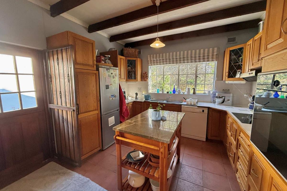 A rustic kitchen featuring exposed timber ceiling beams, fitted wooden cabinetry, granite countertops, and tiled flooring, offering a warm and functional farmhouse aesthetic.