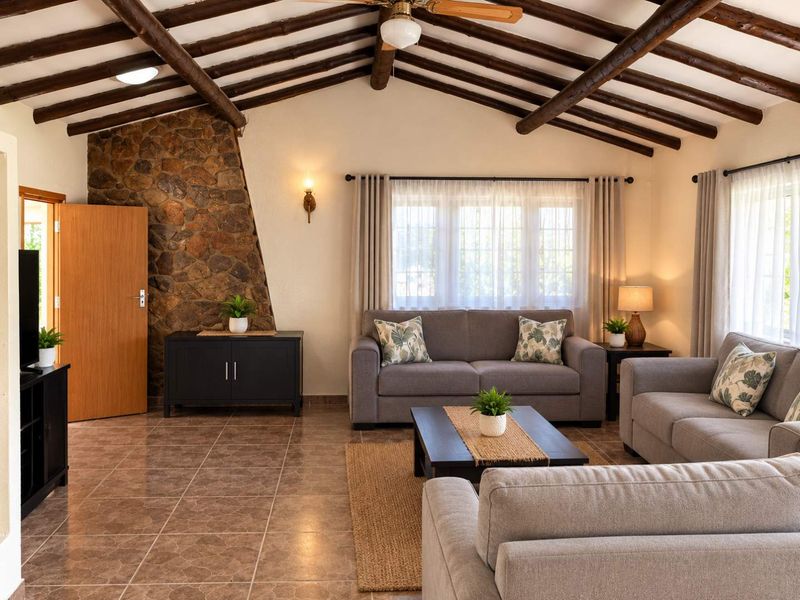 Spacious living room featuring exposed timber ceiling beams, a rustic stone feature wall, and durable tiled flooring, creating a warm and inviting atmosphere.