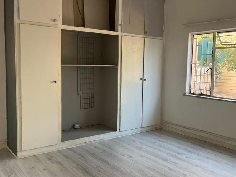 A vacant bedroom featuring laminate flooring, built-in cupboards with storage space, and windows fitted with security bars.