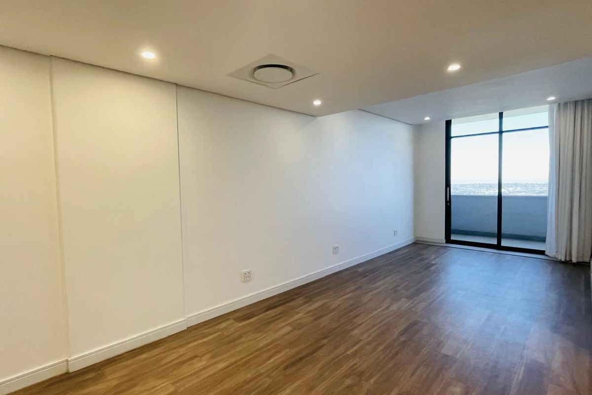 A bright, empty living room featuring modern laminate wood flooring, recessed lighting, ducted air conditioning, and large sliding glass doors leading to a balcony.