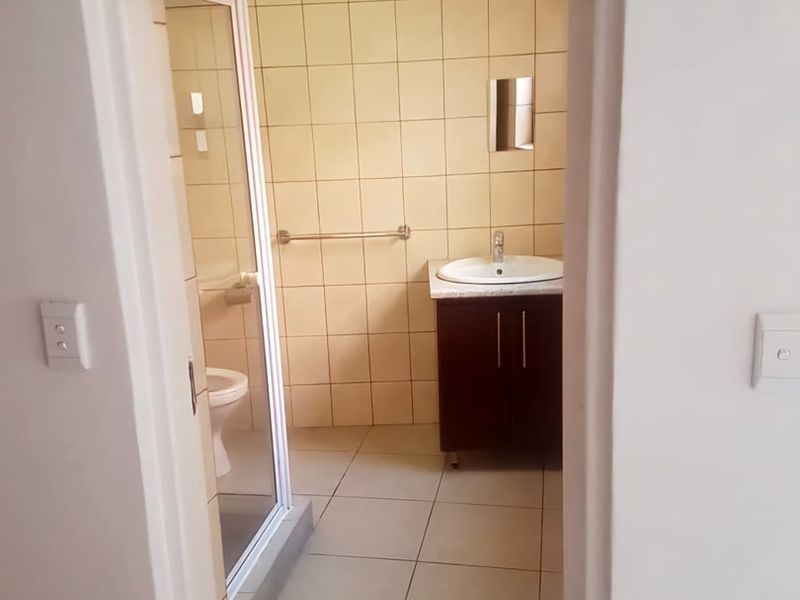 A functional bathroom featuring a vanity cabinet with a basin, a shower enclosure, and a toilet, finished with neutral wall and floor tiles.