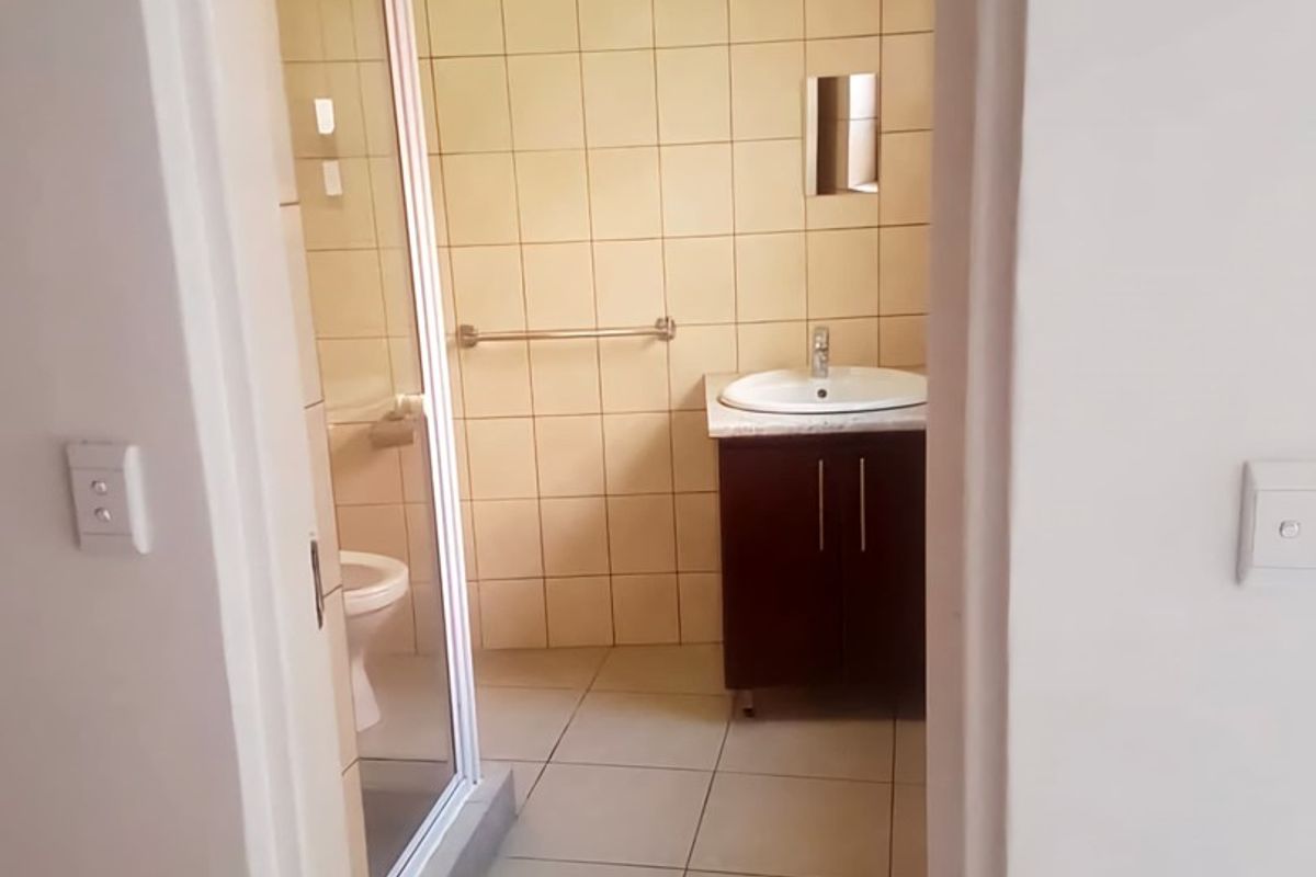 A functional bathroom featuring a vanity cabinet with a basin, a shower enclosure, and a toilet, finished with neutral wall and floor tiles.
