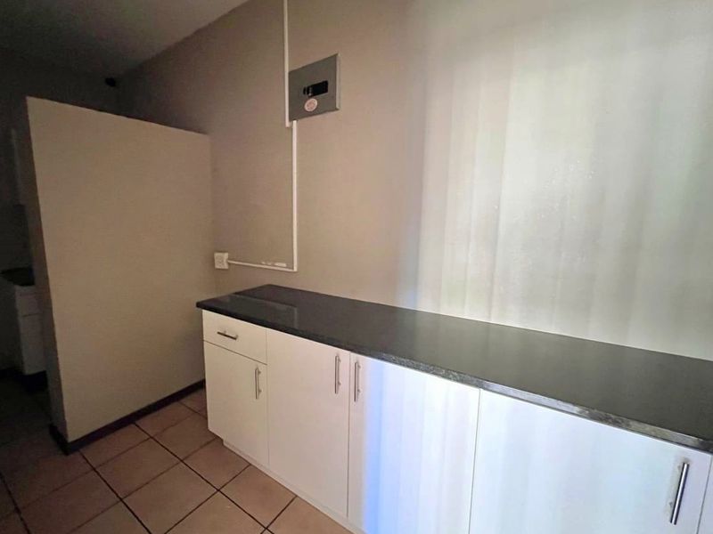 A functional kitchen area featuring white built-in cabinetry, a dark stone countertop, and tiled flooring, suitable for office utility or breakroom use.