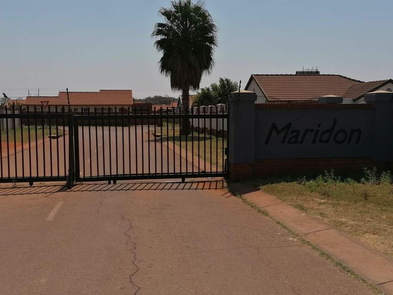 Entrance view of Maridon residential complex featuring a secure gated access point, perimeter walling with electric fencing, and tiled roof housing units.