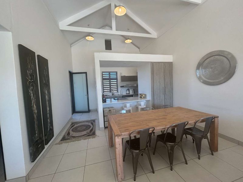 Spacious open-plan living and dining area featuring a vaulted ceiling with exposed trusses, tiled floors, and a modern kitchen with a breakfast bar.