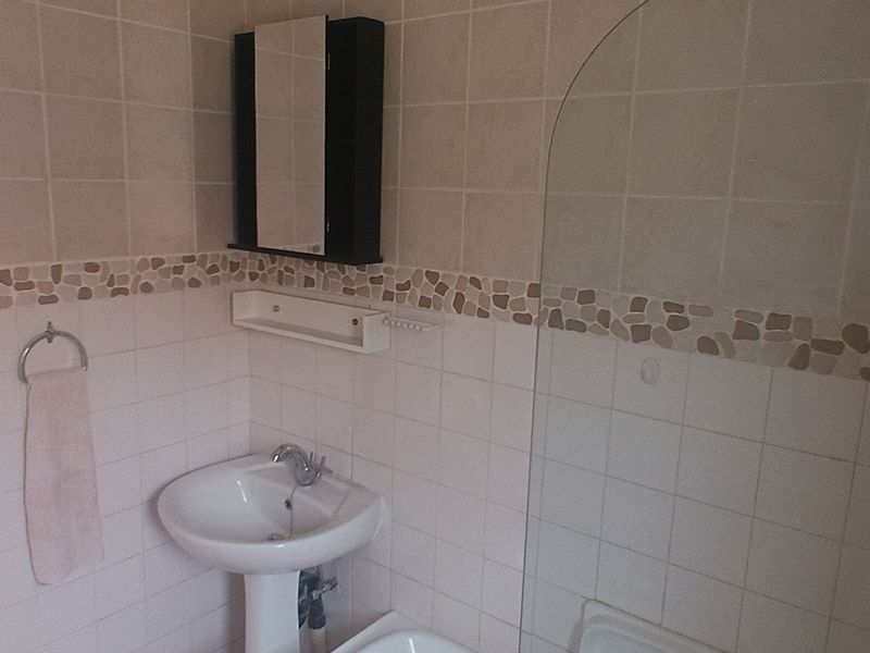 A functional bathroom featuring a pedestal sink, tiled walls with decorative border, and a glass shower screen.