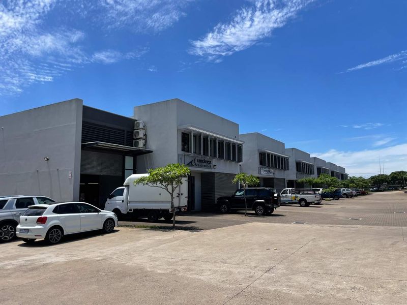 Front elevation of a mixed-use commercial complex featuring multiple units with roller shutter doors, paved parking, and modern architectural detailing.