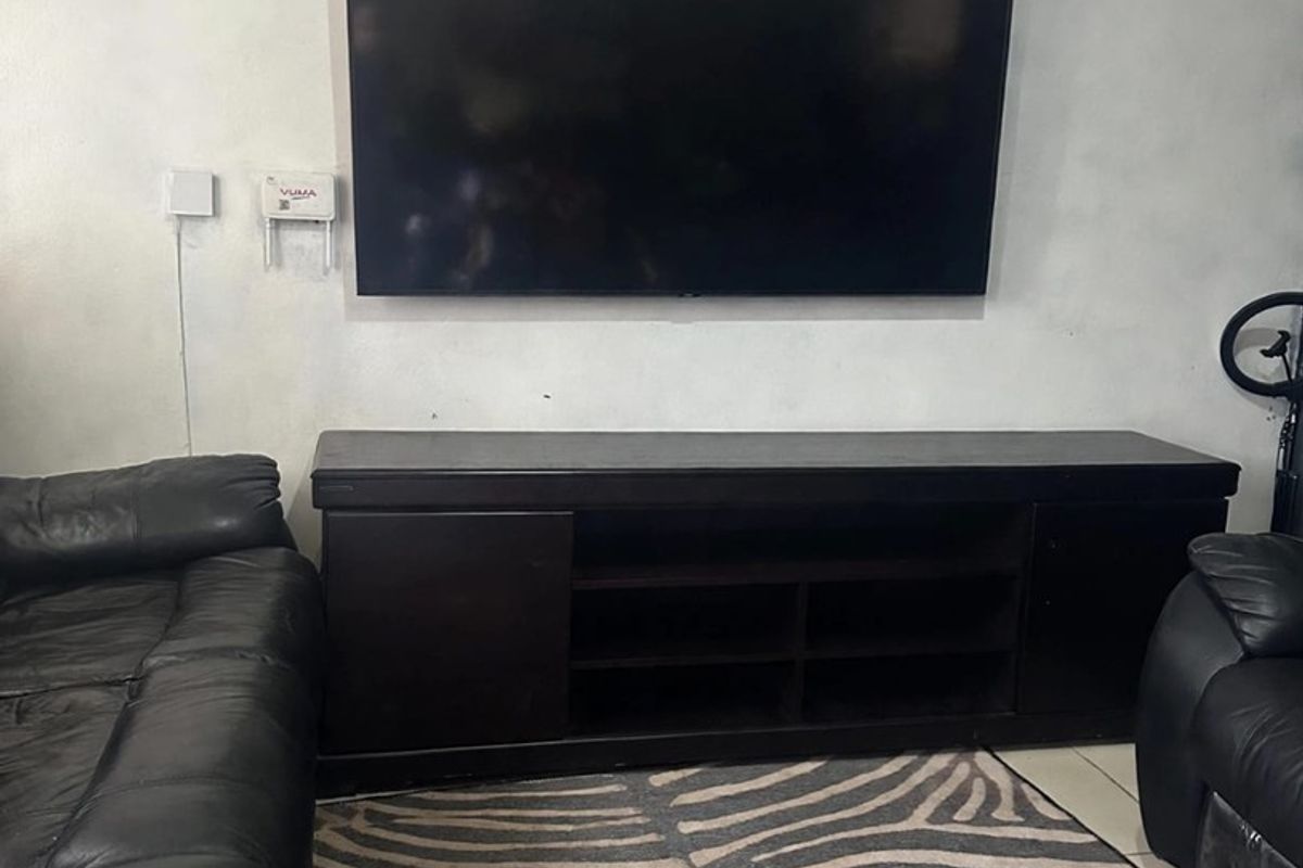 A living room area featuring tiled flooring and wall-mounted electrical points, currently showing signs of wear on the wall surfaces.