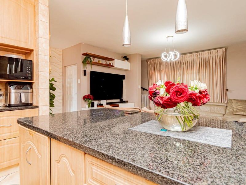 Open plan living area featuring a kitchen with granite island, built-in cabinetry, and modern pendant lighting, flowing into a comfortable lounge space.