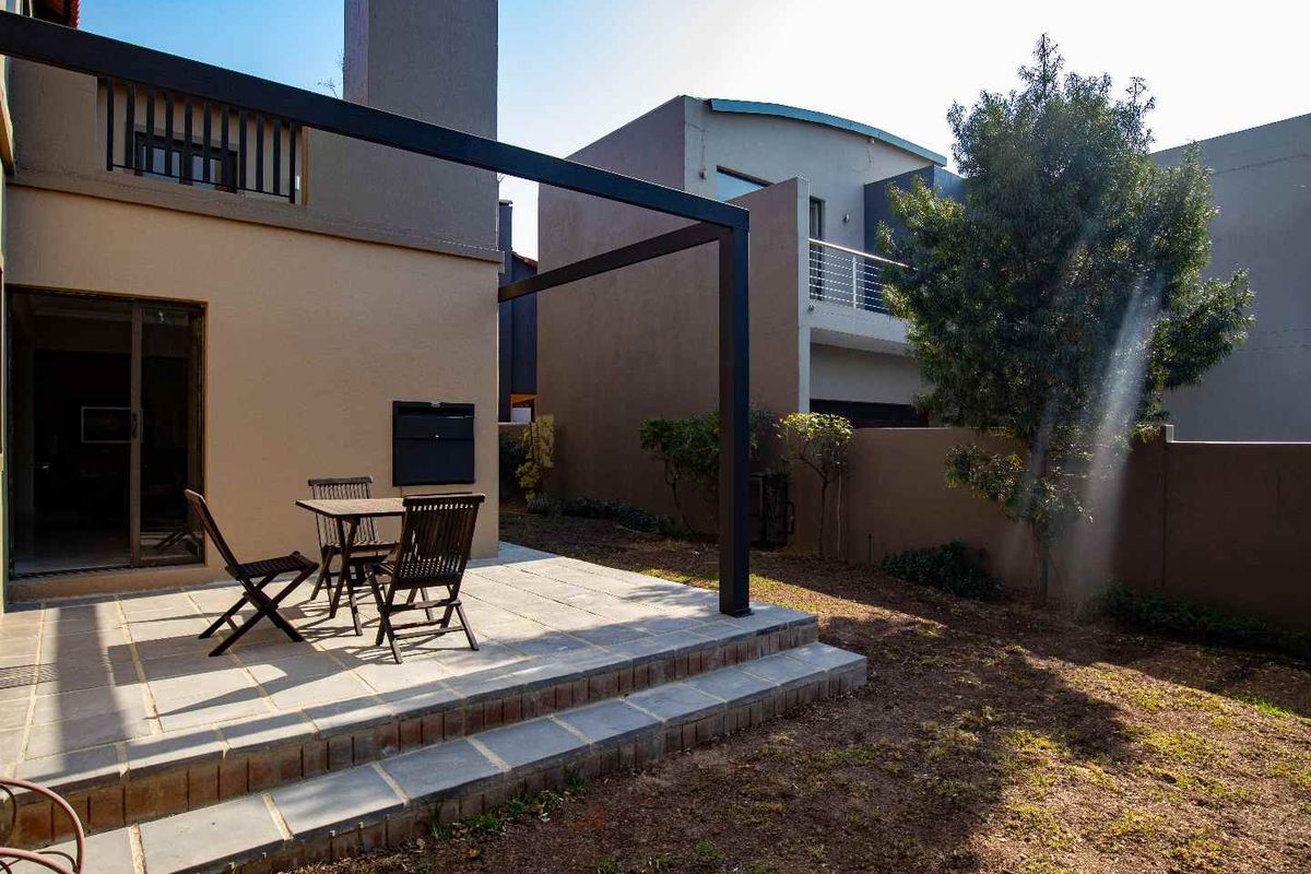 Rear exterior view featuring a paved patio area with a metal pergola, built-in braai, and access to the home via sliding glass doors.