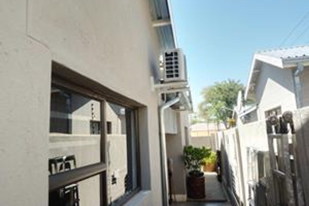 A side exterior view showing a paved walkway, boundary wall, and a wall-mounted air conditioning unit.