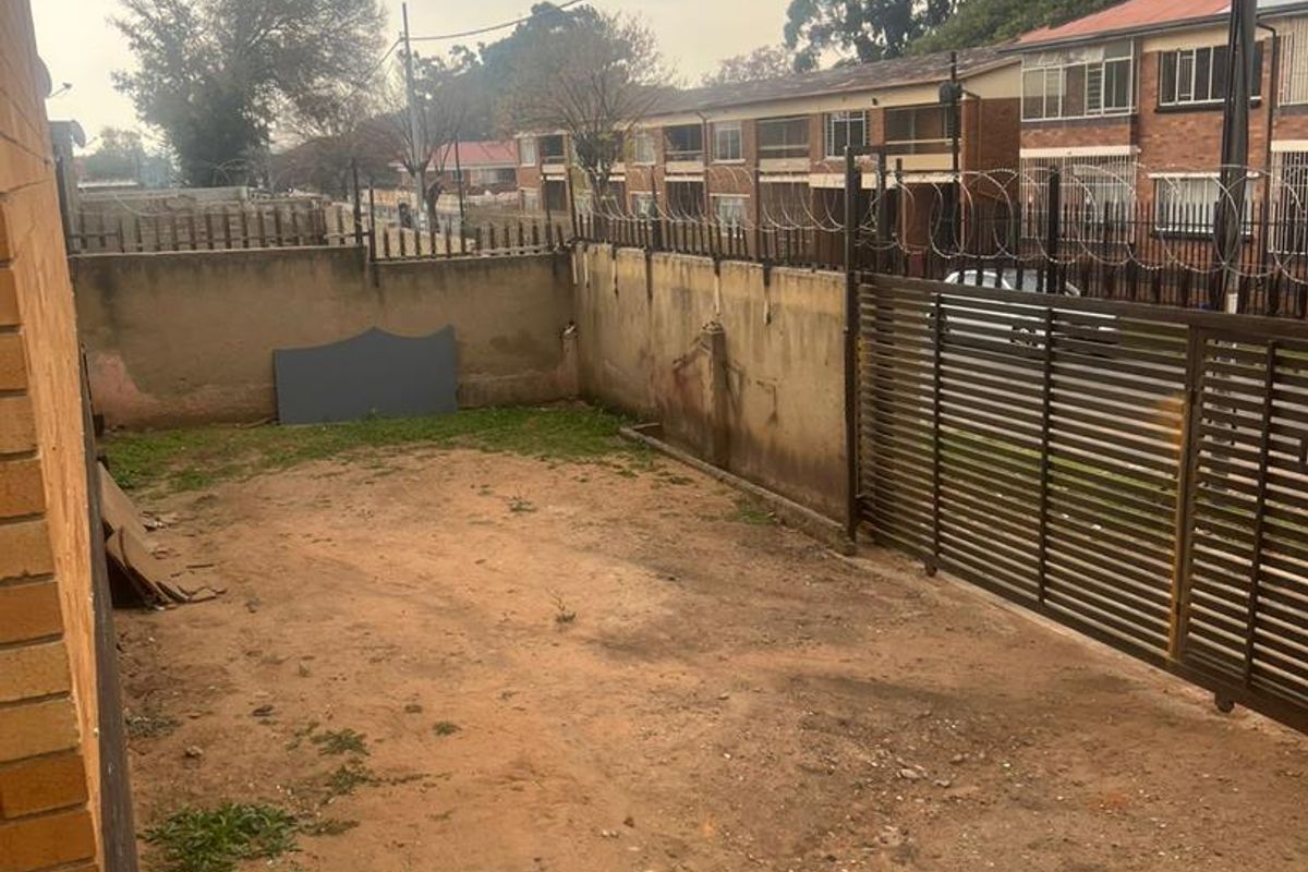 A rear outdoor area featuring a perimeter wall with security razor wire and a sliding metal gate, currently consisting of unpaved ground.