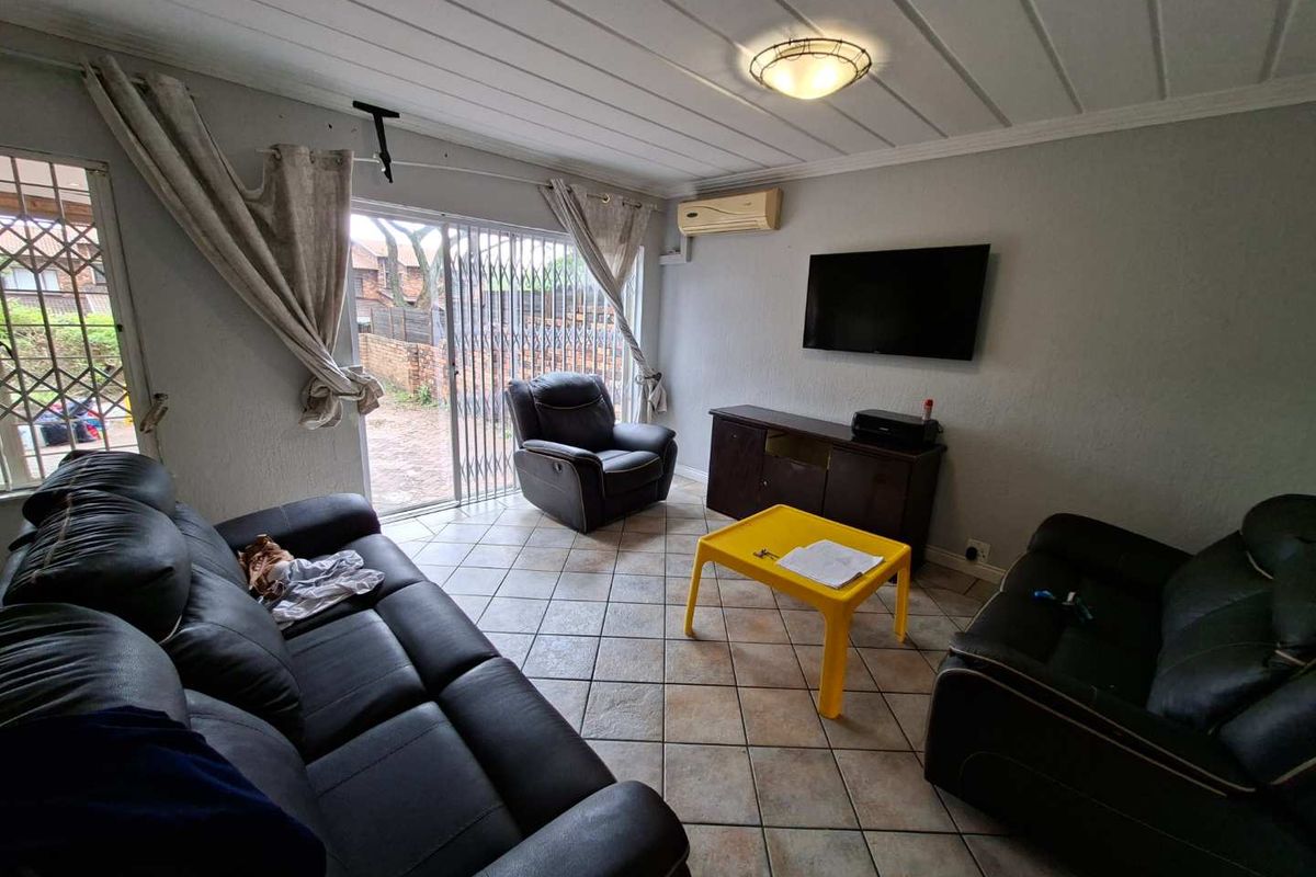 A living room featuring tiled flooring, a split-system air conditioner, and a sliding glass door with security gate leading to the exterior.