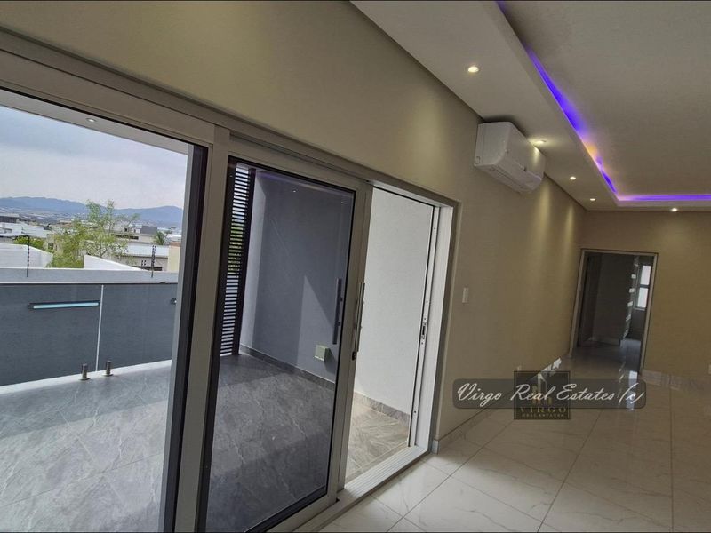 Spacious living area featuring modern tiled floors, recessed ceiling lighting with LED accents, split-system air conditioning, and large sliding doors opening onto a private balcony.