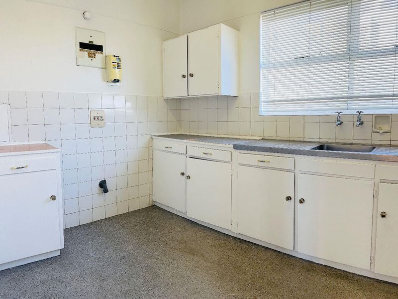 A functional, empty kitchen featuring white built-in cabinetry, a tiled backsplash, and a stainless steel sink, offering a blank canvas for renovation.