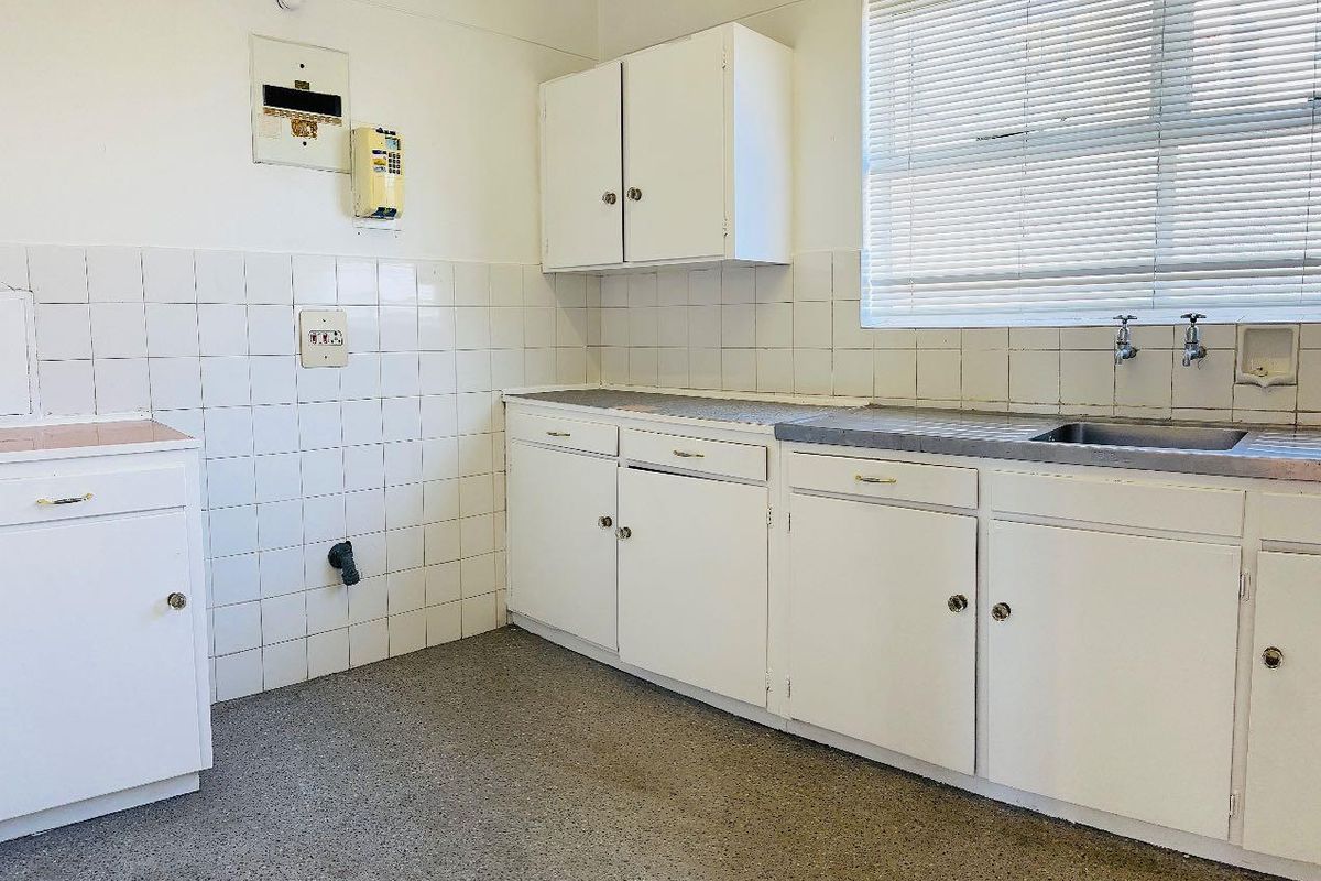 A functional, empty kitchen featuring white built-in cabinetry, a tiled backsplash, and a stainless steel sink, offering a blank canvas for renovation.
