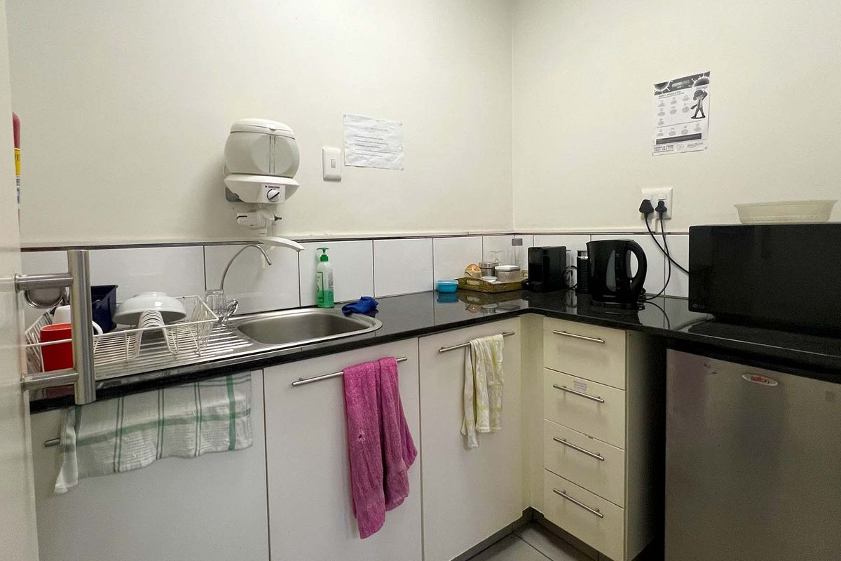 A compact office kitchenette featuring a stainless steel sink, dark granite countertops, and white cabinetry with integrated storage.