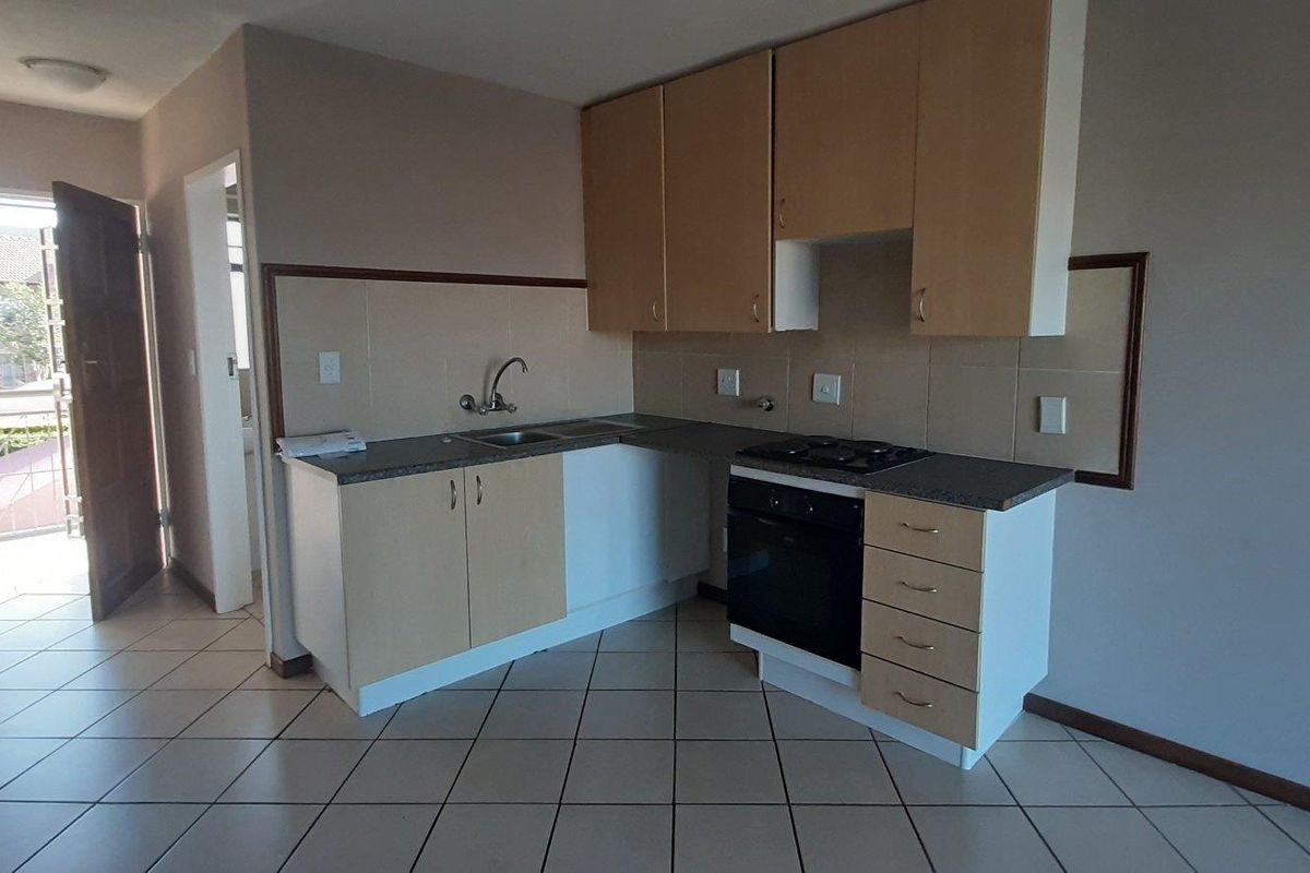 A functional kitchen featuring light wood-finish cabinetry, built-in oven and hob, tiled backsplash, and ceramic floor tiles in an open-plan layout.
