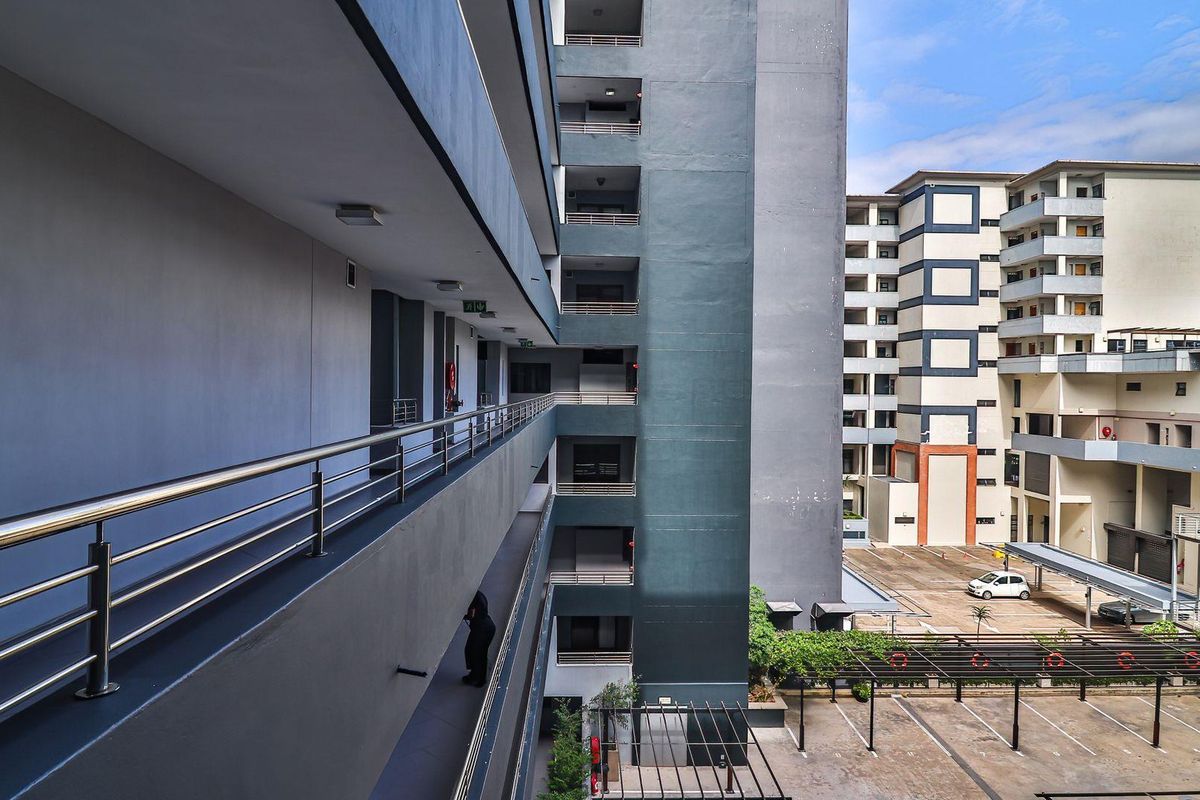 View of the apartment complex exterior, featuring multi-level walkways with stainless steel railings and a paved parking area below.