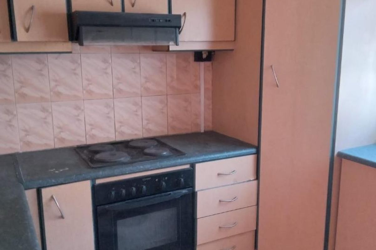 A dated kitchen featuring laminate cabinetry, built-in oven, electric hob, extractor fan, and tiled backsplash with patterned floor tiles.